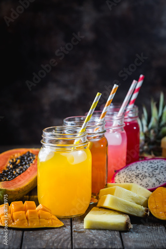 Glasses of tasty fresh tropical juices with fresh tropical fruits, Papaya Pine Apple Mango Dragon on dark background.