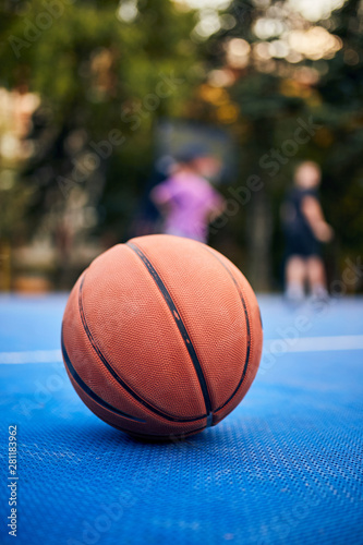 Basketball ball on the urban court with defocused players in background. © astrosystem