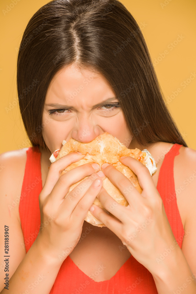 Young greedy woman eating a burger on yellow background Young greedy woman eating a burger on yellow background