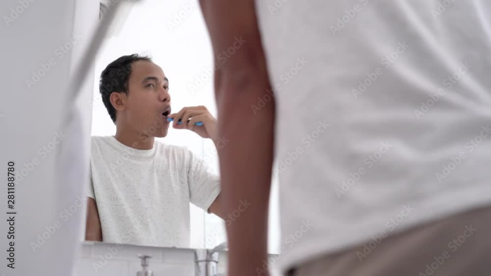 portrait of asian male brushing his teeth at bathroom sink in the morning portrait of asian male brushing his teeth at bathroom sink in the morning