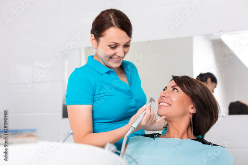 Dentist finishing successful teeth restoration, black haired doctor, in green mask, giving to happy patient mirror, beautiful long-haired woman looking at pristine white teeth with great pleasure