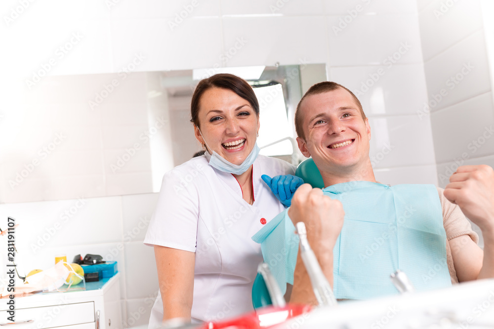 The dentist finishes a successful restoration of teeth, a black-haired doctor with a happy patient looking at the camera. Healthy teeth, brilliant smile.