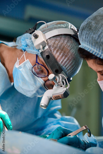 Surgeon and his assistant performing cosmetic surgery on nose in hospital operating room. Nose reshaping, augmentation. Rhinoplasty.