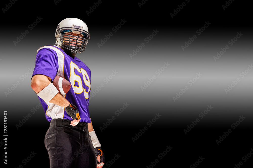American football player in uniform poses for the camera. A handsome athlete in uniform on a black background with a white stripe of light. Copy space, black background. Concept sport, challenge, and