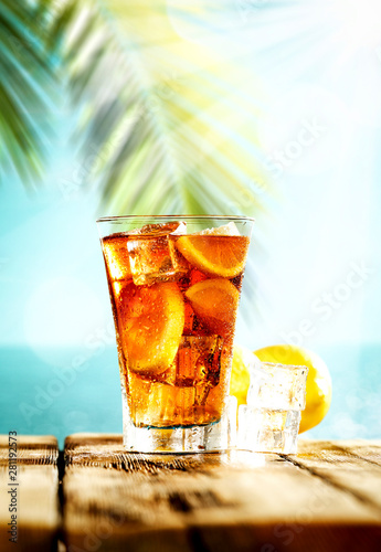 Table background with ice tea on a wooden table top with beautiful blue sky and ocean and palm tree view.