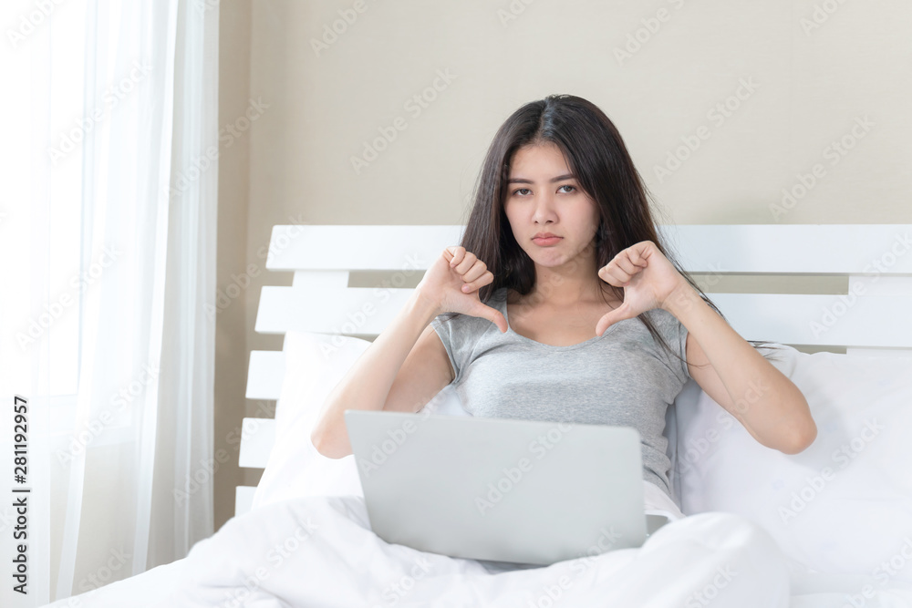 Young beautiful Asian woman sitting on the bed and using laptop computer, she acting with thump down feel upset, copy space Young beautiful Asian woman sitting on the bed and using laptop computer, she acting with thump down feel upset, copy space