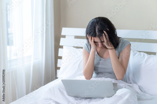 Young beautiful woman sitting on bed, She use laptop feel serious and headache
