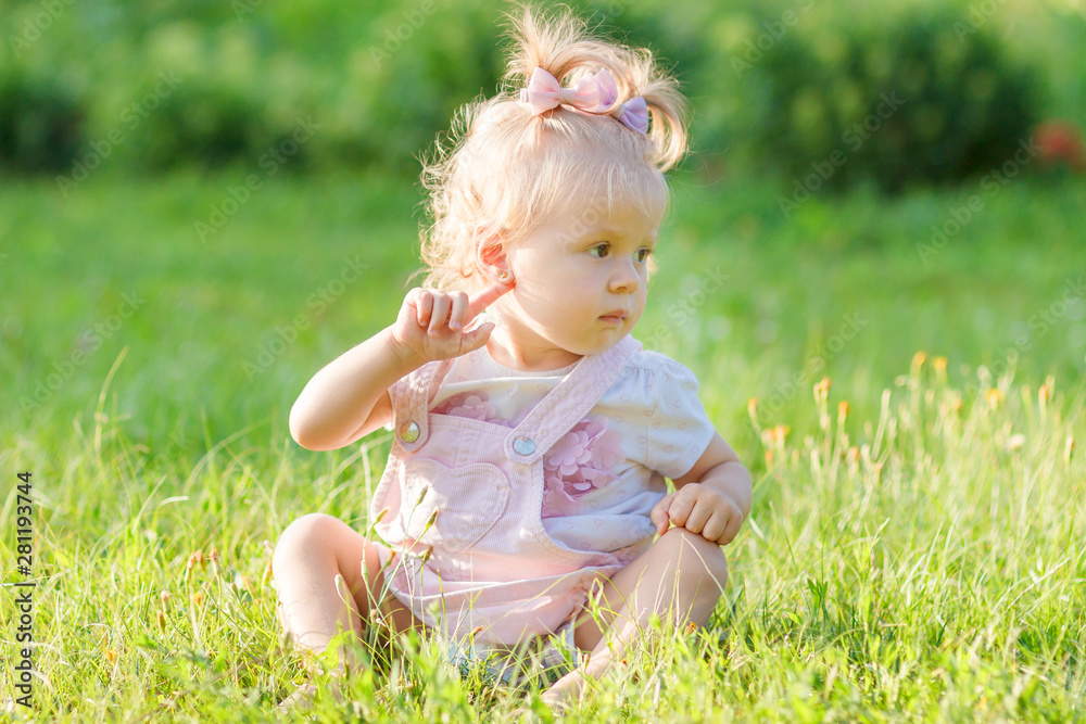 Cute little girl sits on the green grass, outdoors, summer time, blurred background Cute little girl sits on the green grass, outdoors, summer time, blurred background