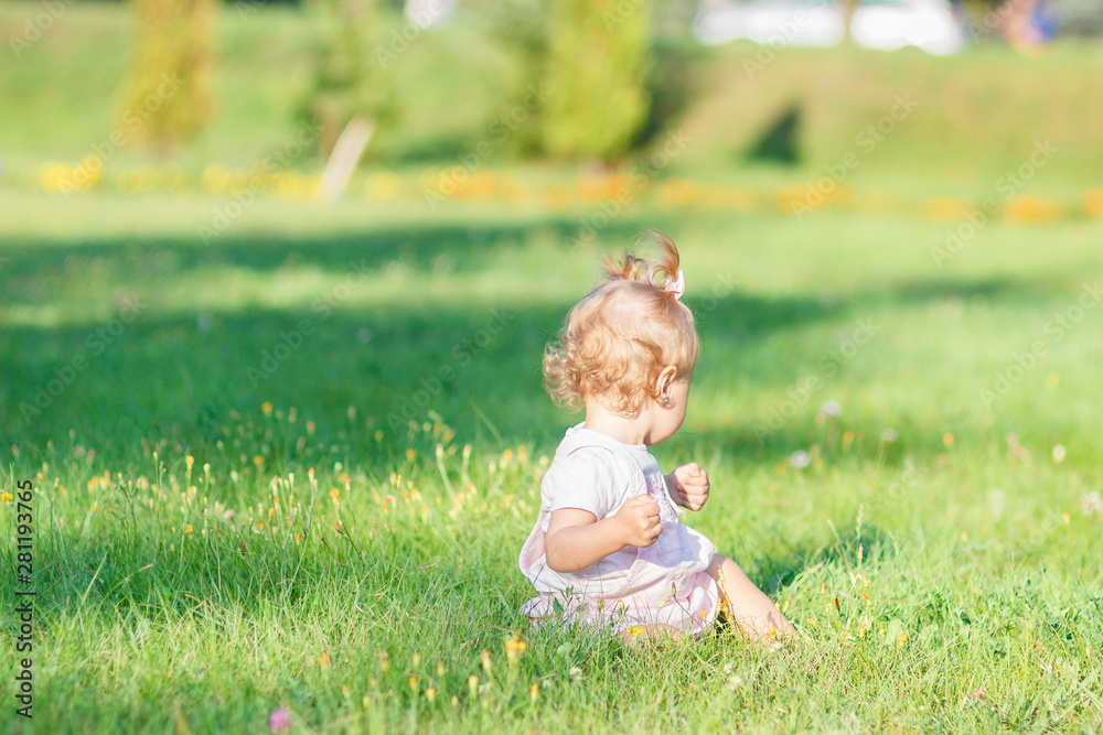 Cute little girl sits on the green grass, outdoors, summer time, blurred background Cute little girl sits on the green grass, outdoors, summer time, blurred background