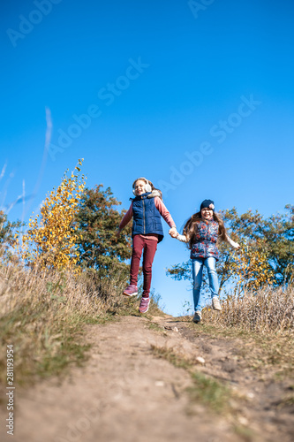 Teen girls run, holding hands, in the autumn park. Sisters having fun on a nature. Two little girlfriends. Happy and healthy childhood.