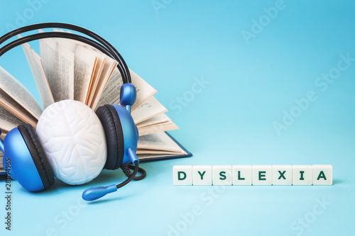 Dyslexia word with an open book and brain stress relief in headphones on blue background, reading difficulty and disorder and auditory memory concept. Education and neurology with copy space photo