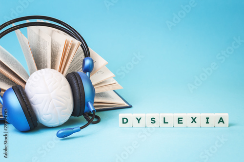 Bilde på lerret Dyslexia word with an open book and brain stress relief in headphones on blue background, reading difficulty and disorder and auditory memory concept