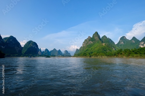 Wide angle of green mountains above blue water. Sunny blue sky white clouds. At the Lijiang ( Li river) in Yangshuo Guilin city China. Karst landform