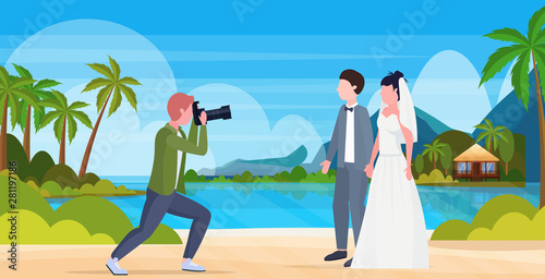 professional wedding photographer shooting on camera newly weds couple bride and groom embracing tropical island summer sea beach seaside landscape background full length flat horizontal