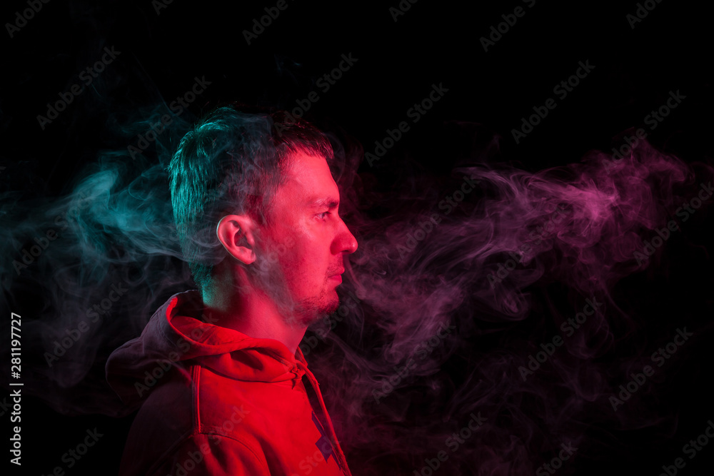 Portrait of a man in profile face looking on a black isolated background with a feeling of sadness and loneliness, around the head a cloud of green and pink smoke. The soul and feelings.