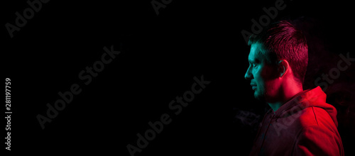 Close-up of the face of an unshaven face of a caucasian man looking away with stubble in the dark, illuminated on one side in Blue and on the other pink on a black isolated background. Cyberpunk style