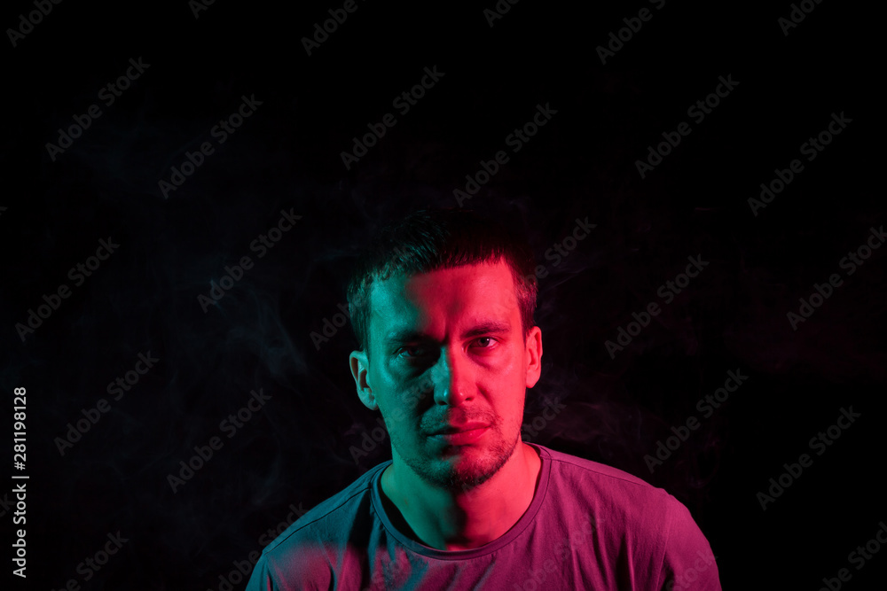 Portrait of a man in profile face on a black isolated background with a feeling of sadness and loneliness, around the head a cloud of blue and pink smoke. The soul and feelings.