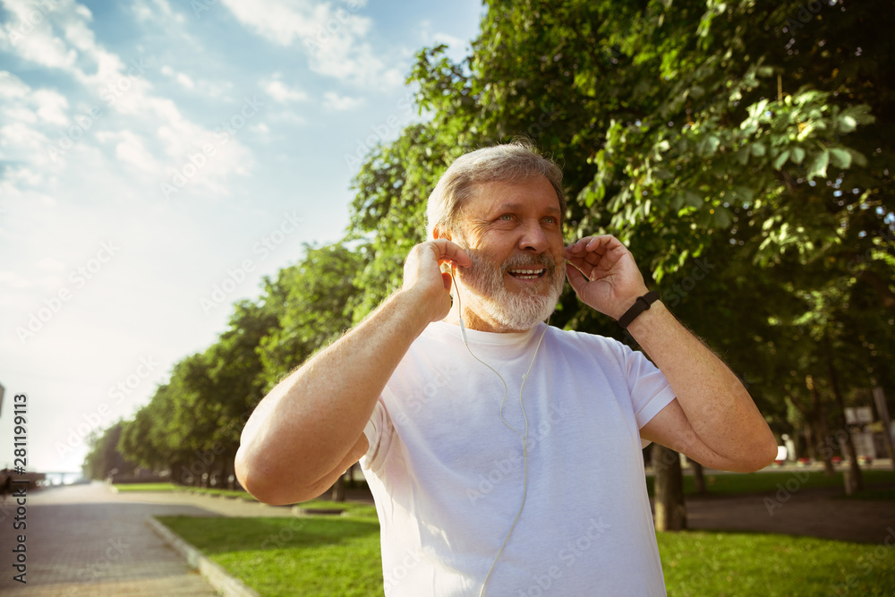 Senior man as runner with fitness tracker at the city's street. Caucasian male model using gadgets while jogging and cardio training in summer's morning. Healthy lifestyle, sport, activity concept. Senior man as runner with fitness tracker at the city's street. Caucasian male model using gadgets while jogging and cardio training in summer's morning. Healthy lifestyle, sport, activity concept.