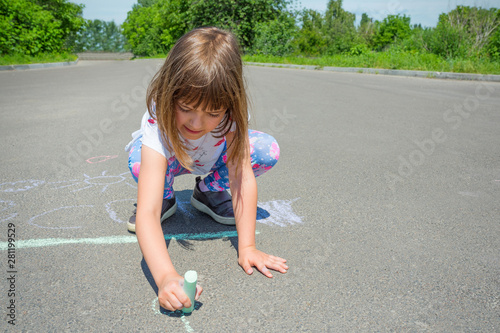 A little girl draws with chalk on an asphalt road. Concept - children's drawings of a picture on asphalt.