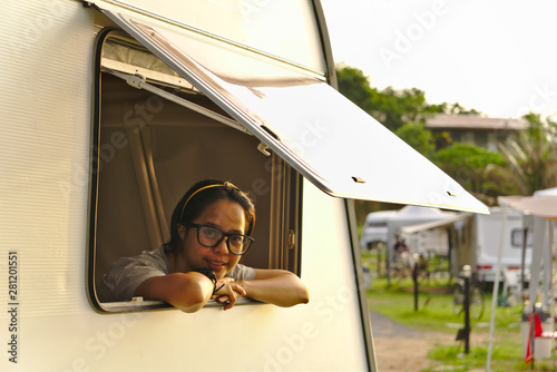Young asian female wearing black glasses sitting and smiling from campervan windows in the morning with the warm light