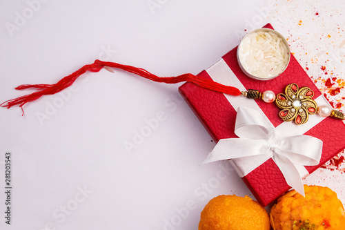 Raksha Bandhan concept– Close view of sprinkles of kumkum and haldi with elegant rakhi on red gift box with sweets on white background