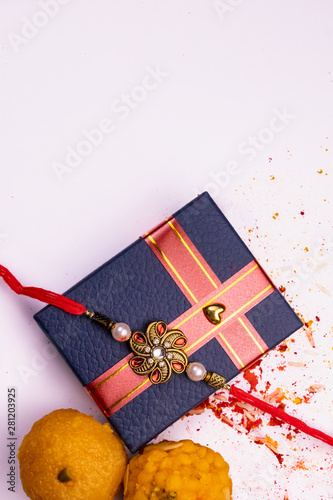 Top view of sprinkled rice, kumkum, haldi with elegant rakhi on blue gift box and sweets on white surface