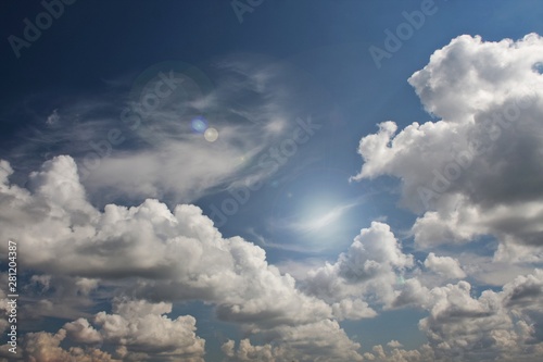 Białe chmury z flarą słoneczną na niebieskim niebie