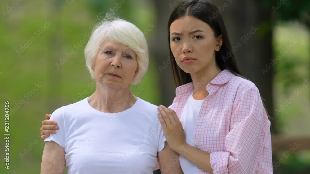 Upset young woman with grandmother looking at camera outdoors, social support Upset young woman with grandmother looking at camera outdoors, social support