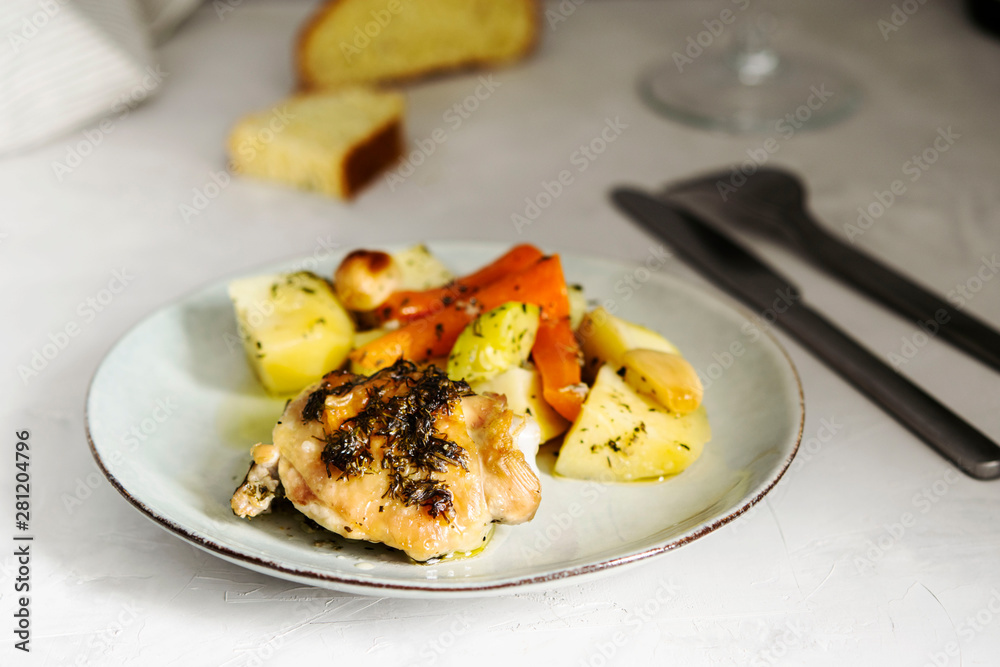 Homemade herb and spice chicken thighs baked with vegetables on a plate on grey background. Homemade lunch. Selective focus Homemade herb and spice chicken thighs baked with vegetables on a plate on grey background. Homemade lunch. Selective focus