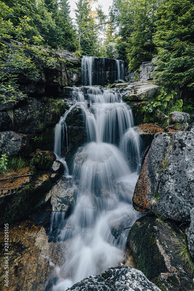 Obraz premium Waterfall photograph. Long exposure photo of a beautiful waterfall of Jedlova, Jizerske mountains, Czechia. Motion blurr water in a mountain creek in a deep forest. Alaska like stream with a rocks.