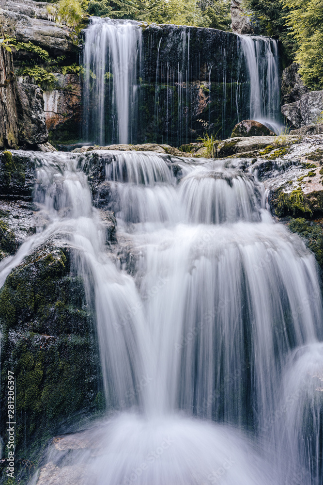 Fototapeta premium Waterfall photograph. Long exposure photo of a beautiful waterfall of Jedlova, Jizerske mountains, Czechia. Motion blurr water in a mountain creek in a deep forest. Alaska like stream with a rocks.