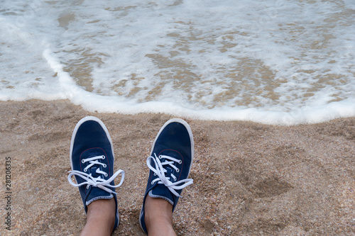 woman foot in blue casual sneaker shoes on the beach with sea water foam summer vacation background