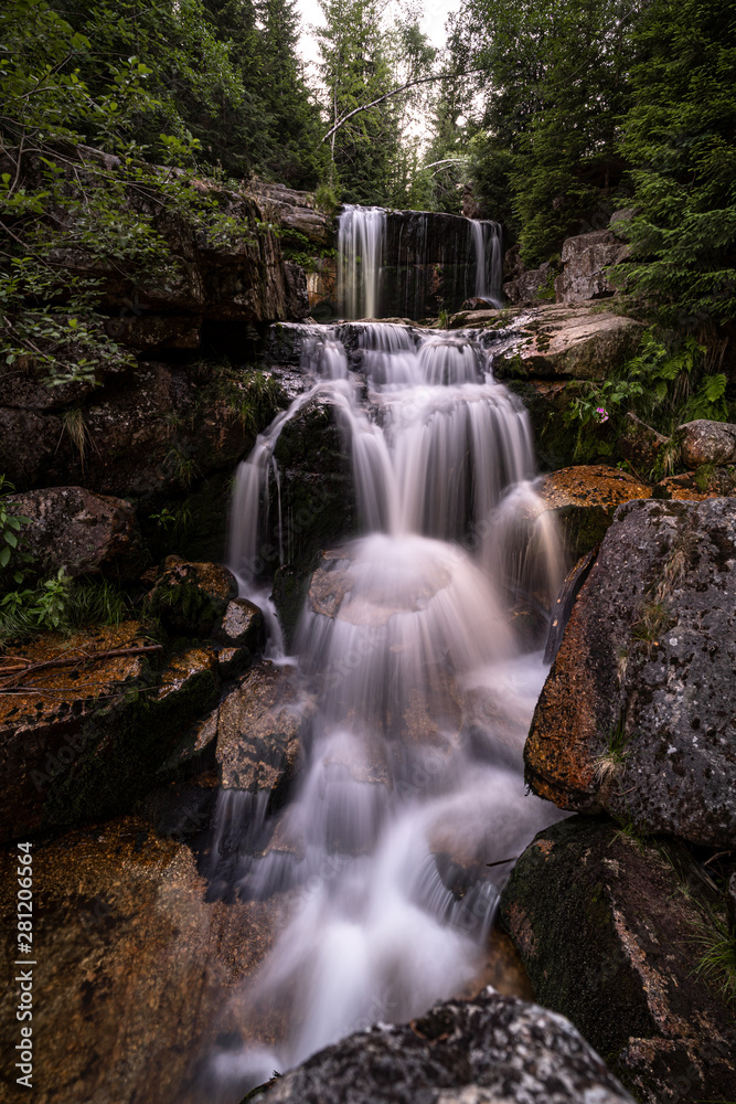 Fototapeta premium Waterfall photograph. Long exposure photo of a beautiful waterfall of Jedlova, Jizerske mountains, Czechia. Motion blurr water in a mountain creek in a deep forest. Alaska like stream with a rocks.