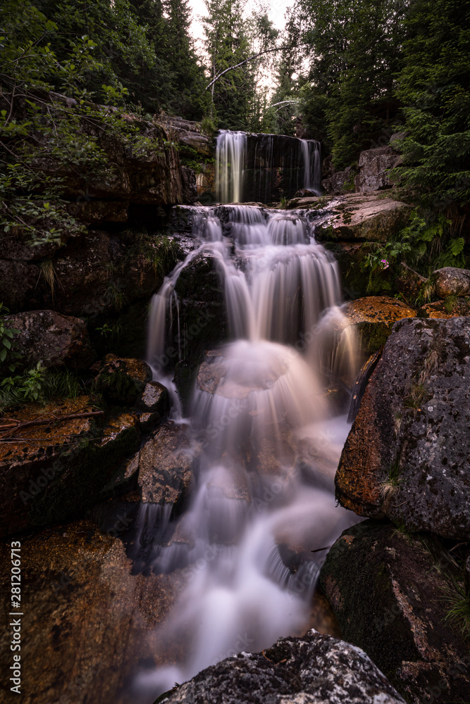 Fototapeta premium Waterfall photograph. Long exposure photo of a beautiful waterfall of Jedlova, Jizerske mountains, Czechia. Motion blurr water in a mountain creek in a deep forest. Alaska like stream with a rocks.