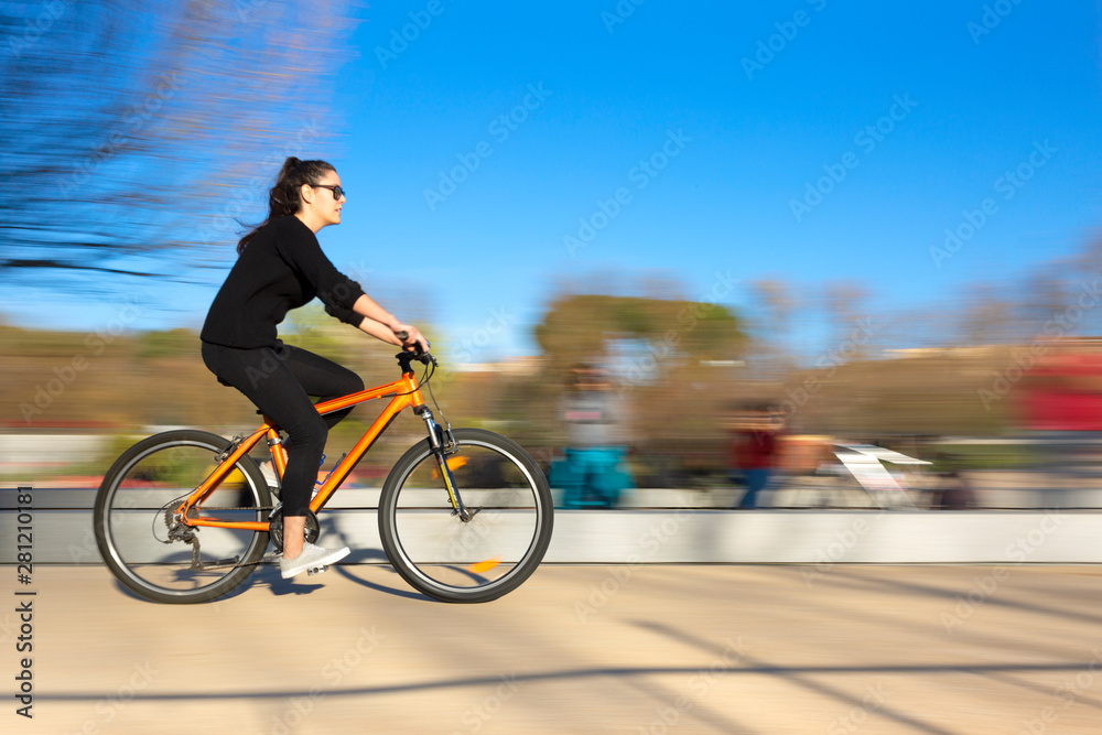 Chica joven vestida de negro montando en bicicleta en el parque