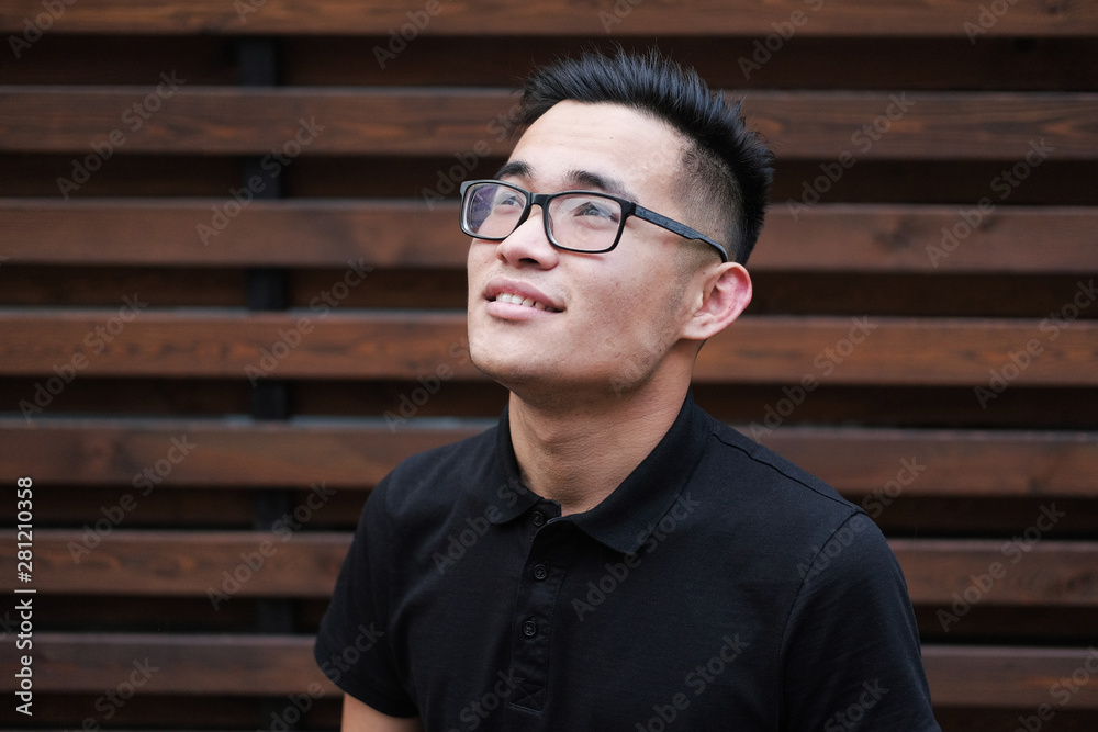 A young korean man in a black t-shirt. Asian man with glasses on a wooden background. A young korean man in a black t-shirt. Asian man with glasses on a wooden background.