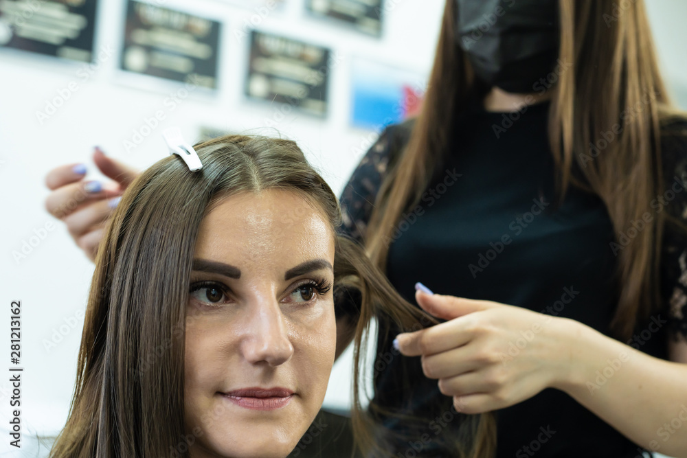 Fototapeta premium hairdresser makes hair lamination in a beauty salon for a girl with brunette hair. hair care concept.