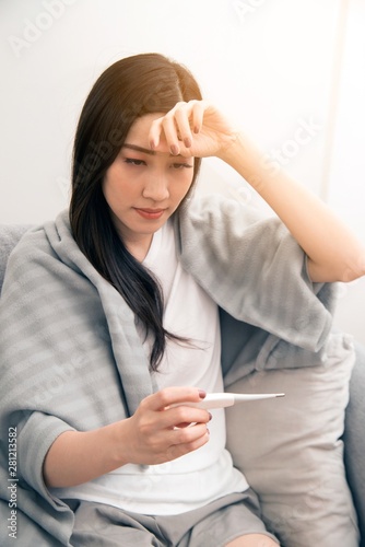 Asian woman sick from cold and used with thermometer suffering on sofa in the room..