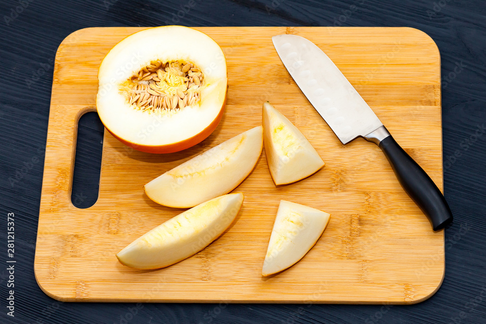 Half a yellow melon and slices sliced with a knife on a cutting Board, on a black wooden background. Half a yellow melon and slices sliced with a knife on a cutting Board, on a black wooden background.