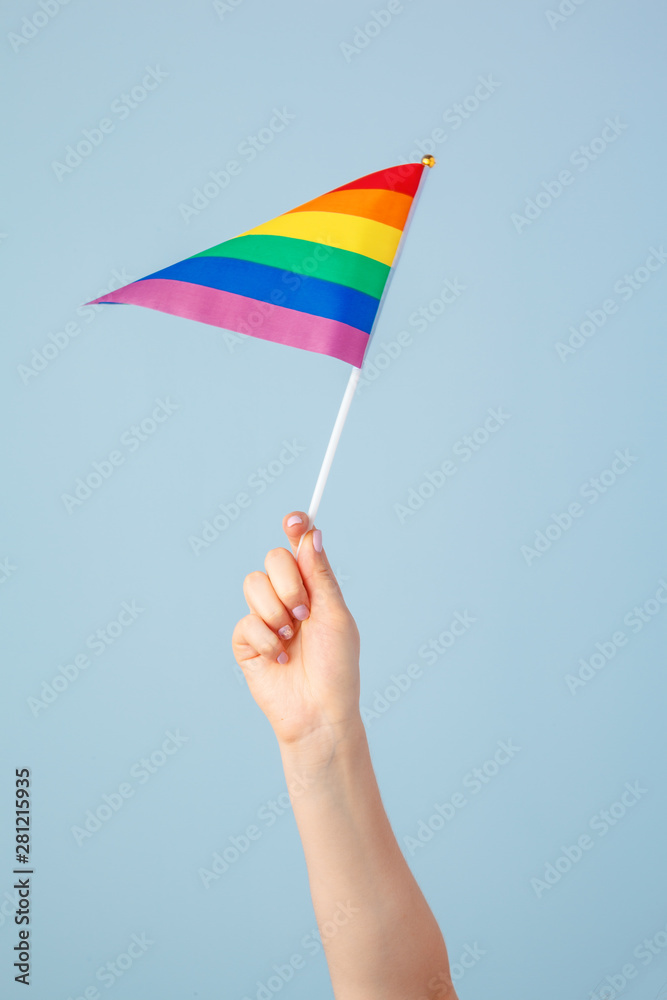 Closeup of a hand waving a small rainbow flag against a light blue background Closeup of a hand waving a small rainbow flag against a light blue background