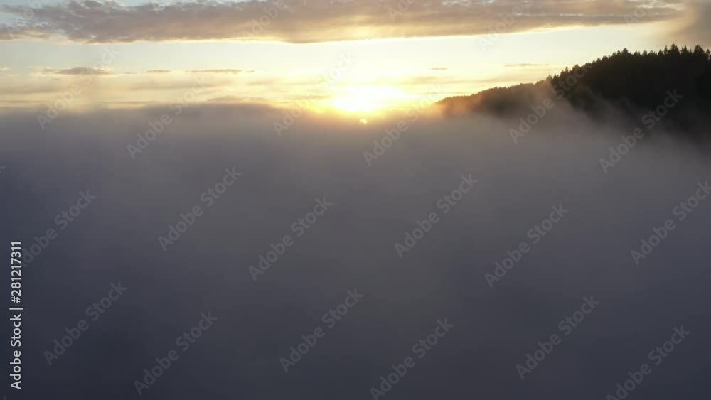 A golden sunset peaking through dense fog over tree filled mountains A golden sunset peaking through dense fog over tree filled mountains