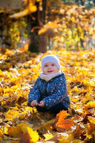 smiling baby girl sitting in yellow leaves