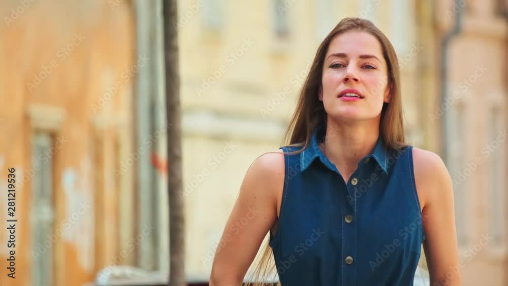 Inspired caucasian girl admiring modern cityscape walking in the street on lovely day. Portrait of pleasant pretty woman in blue stylish dress outdoors. Urban lifestyle. Inspired caucasian girl admiring modern cityscape walking in the street on lovely day. Portrait of pleasant pretty woman in blue stylish dress outdoors. Urban lifestyle.