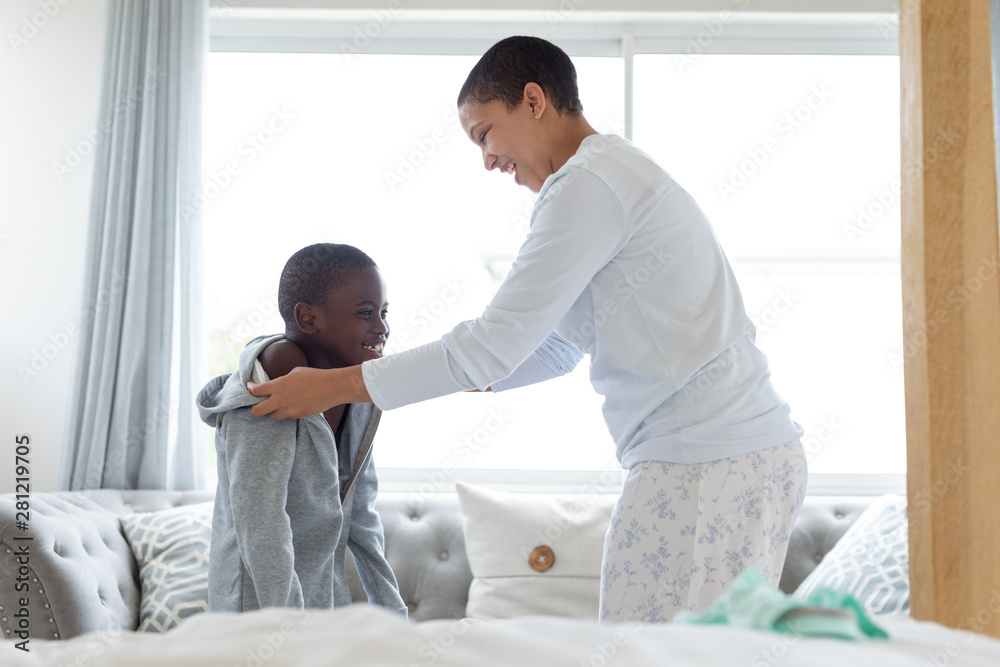 Mother helping her son to wear clothes in bedroom Mother helping her son to wear clothes in bedroom