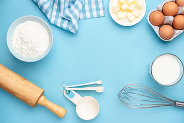 Baking ingredients eggs flour butter rolling pin whisker milk for bread, pastry or cake on blue background with copy space for text