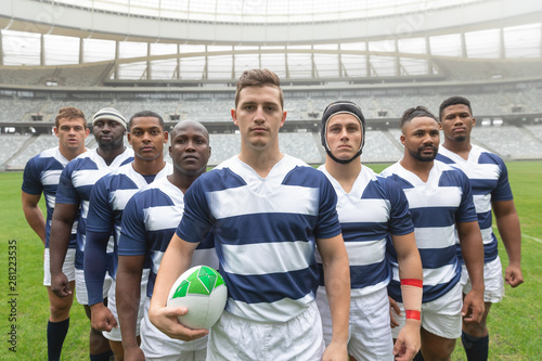 Group of diverse male rugby players standing together with rugby ball in stadium photo