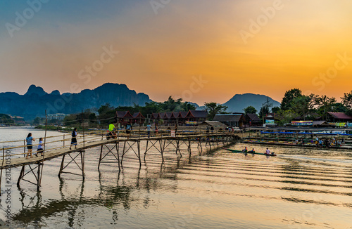 Vang Vieng, Laos - February 2019: Unidentified tourist walking on bamboo bridge over Nam Song River with mountain sunset background 