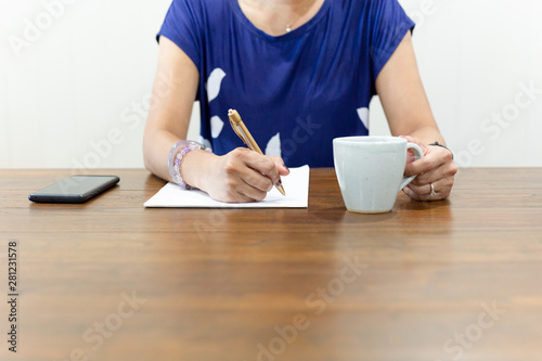Businesswoman hand writing on paperwork with cup of coffee on working desk.