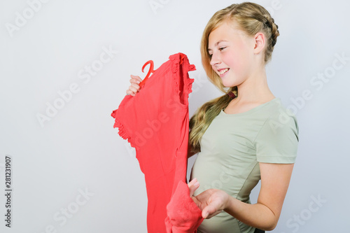 Teen blonde girl choosing a dress for fitting. Fitting clothes. Caucasian girl holding a orange dress on a hanger. photo