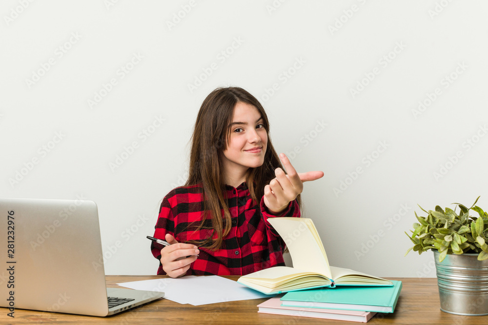 Young teenager going back to her routine doing homeworks pointing with finger at you as if inviting come closer. Young teenager going back to her routine doing homeworks pointing with finger at you as if inviting come closer.